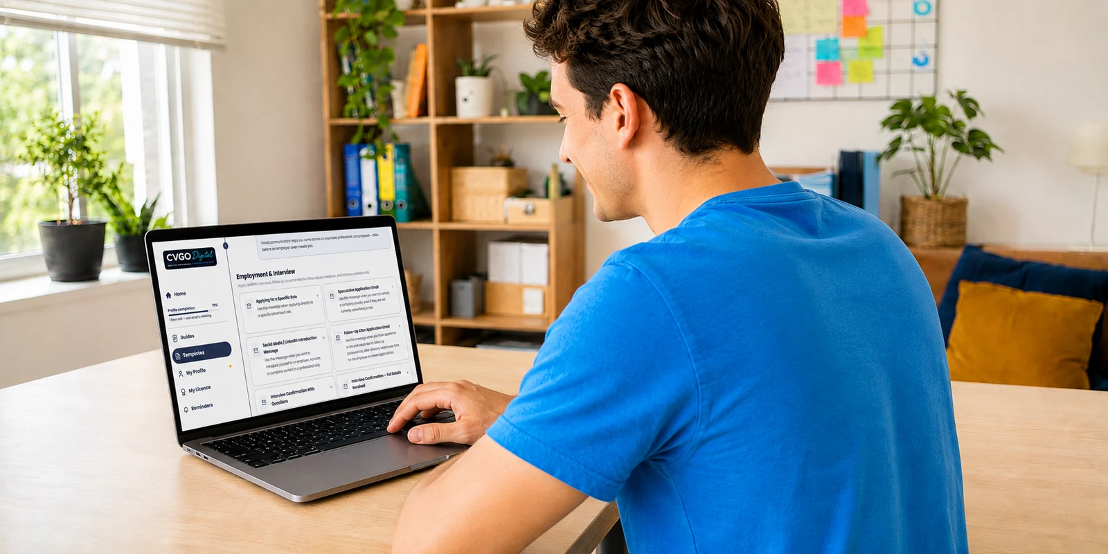 The same young man at the same desk, now sitting up and smiling, with CVGO Digital open on his laptop.